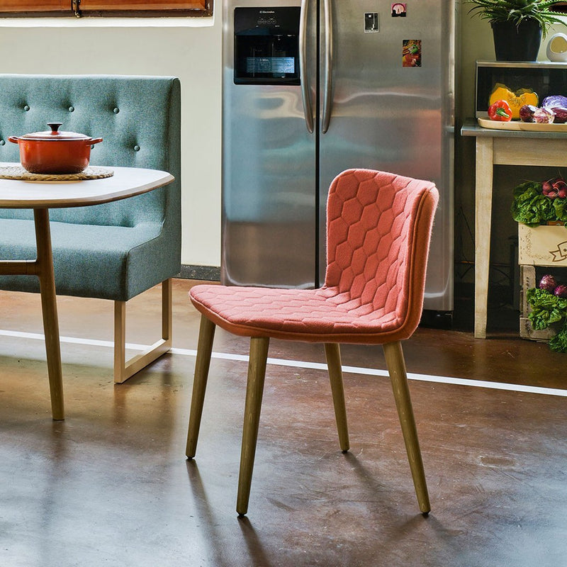 Coral quilted dining chair with wooden legs, complemented by a soft teal upholstered table and modern kitchen decor.