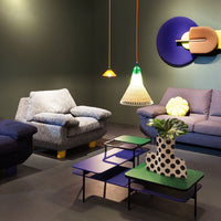 Colorful living space featuring blue patterned sofas, vibrant green and purple tables, and unique yellow and green lighting.