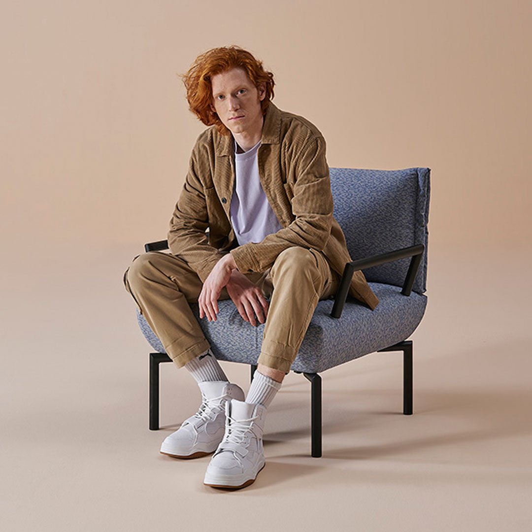 Casual beige outfit paired with a textured blue chair against a soft peach background.