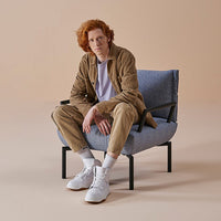 Casual beige outfit paired with a textured blue chair against a soft peach background.