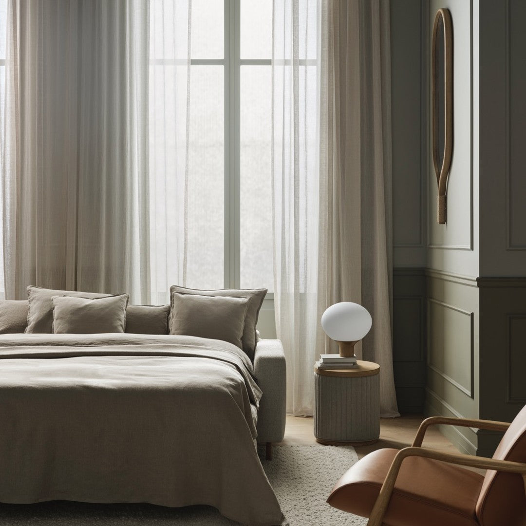 Neutral beige bedding with soft texture, sheer light curtains, and warm wood accents against a muted green wall.