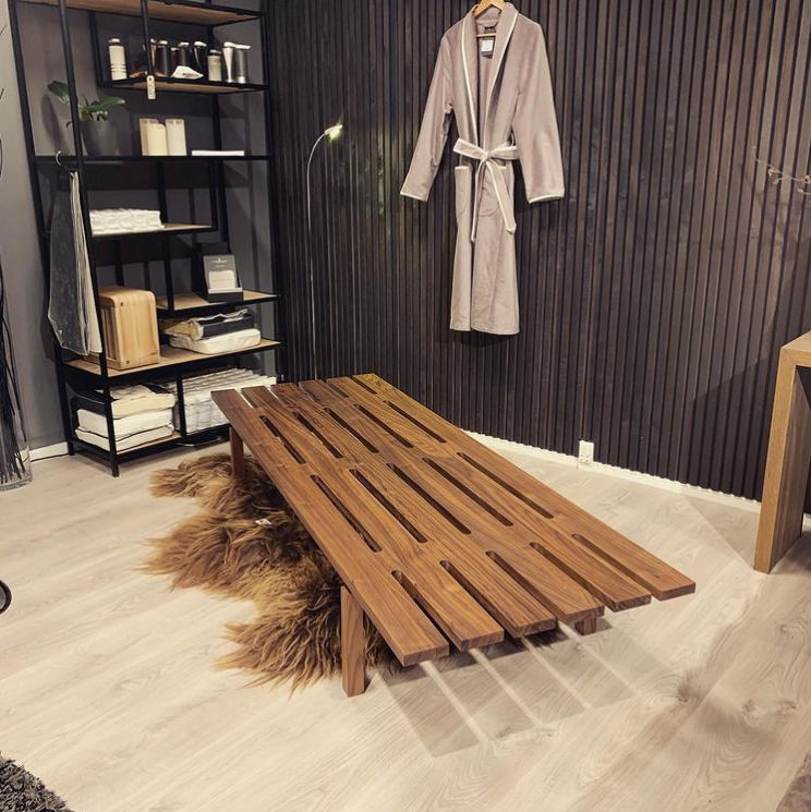 Brown wooden slatted coffee table on light wood floor, with a modern, minimalist design against a dark, textured wall.