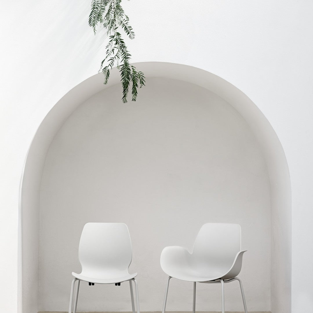 Minimalist white chairs against a smooth, curved white wall with green foliage accents.