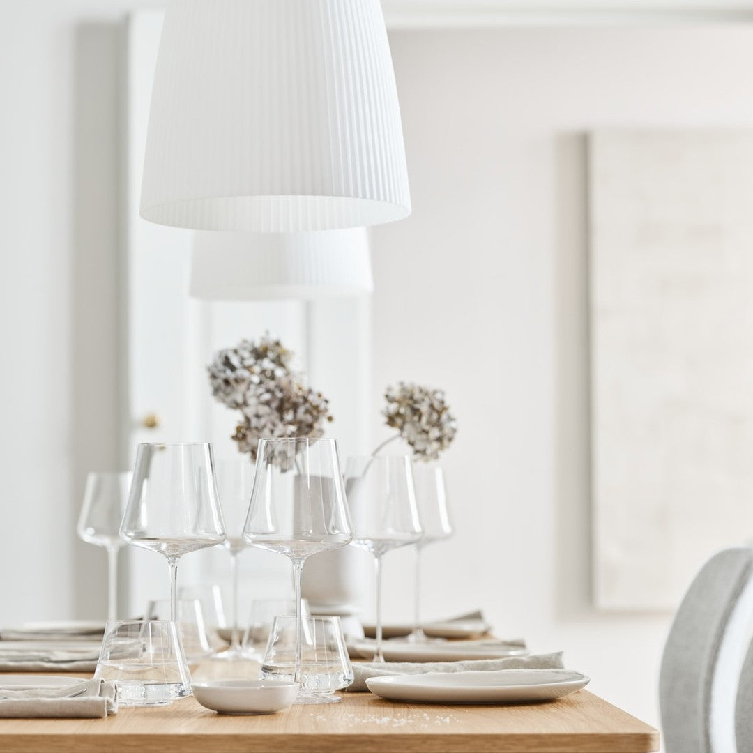 "Rustic wooden table set with clear glassware, neutral plates, and white decor elements in a soft, minimalist setting."