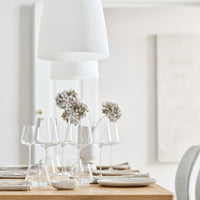 "Rustic wooden table set with clear glassware, neutral plates, and white decor elements in a soft, minimalist setting."