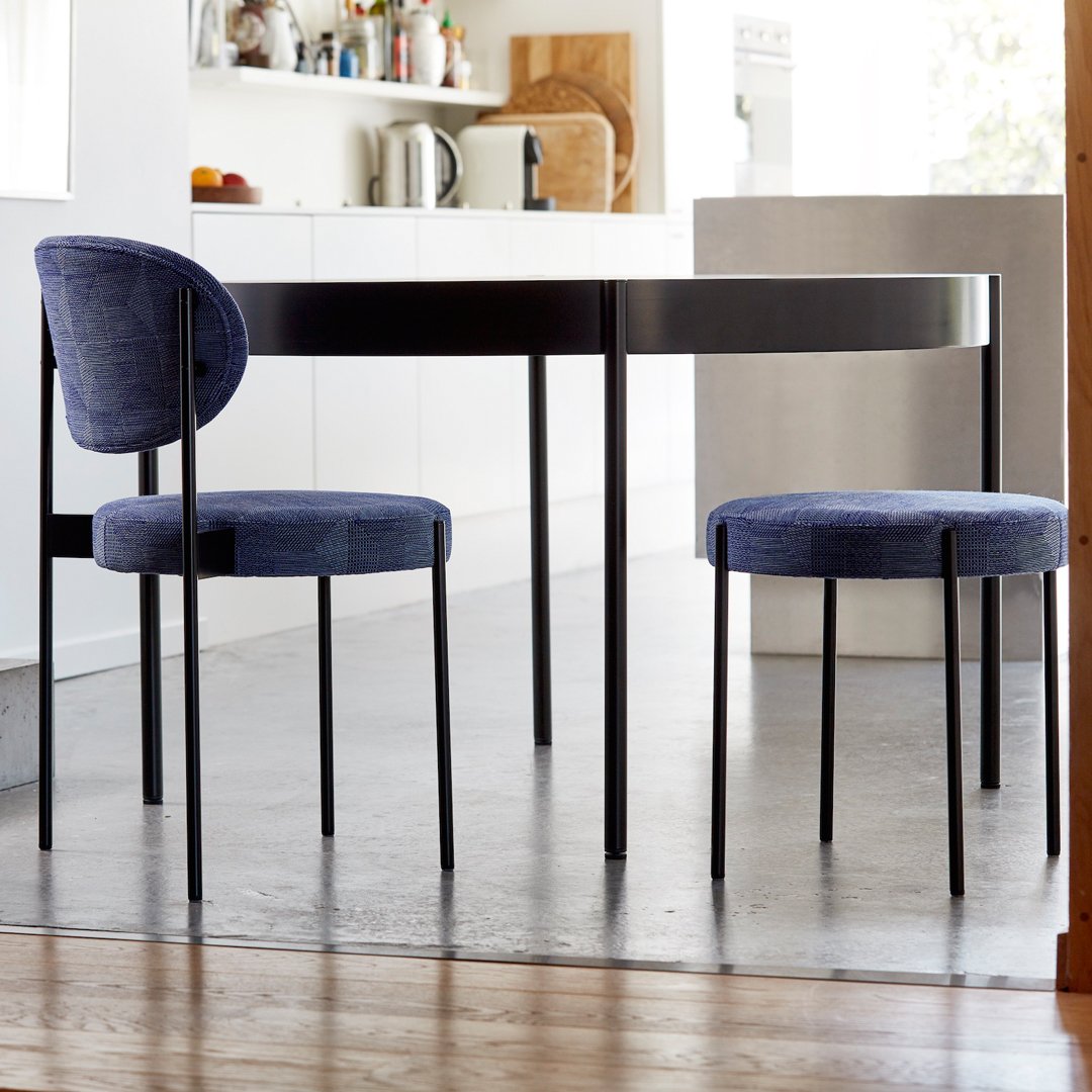 Stylish round table with sleek black finish and modern blue upholstered chairs in a bright, minimalist kitchen setting.