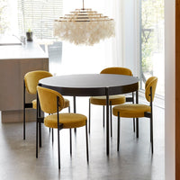 Round black dining table with four mustard yellow upholstered chairs, set in a modern interior with soft lighting.