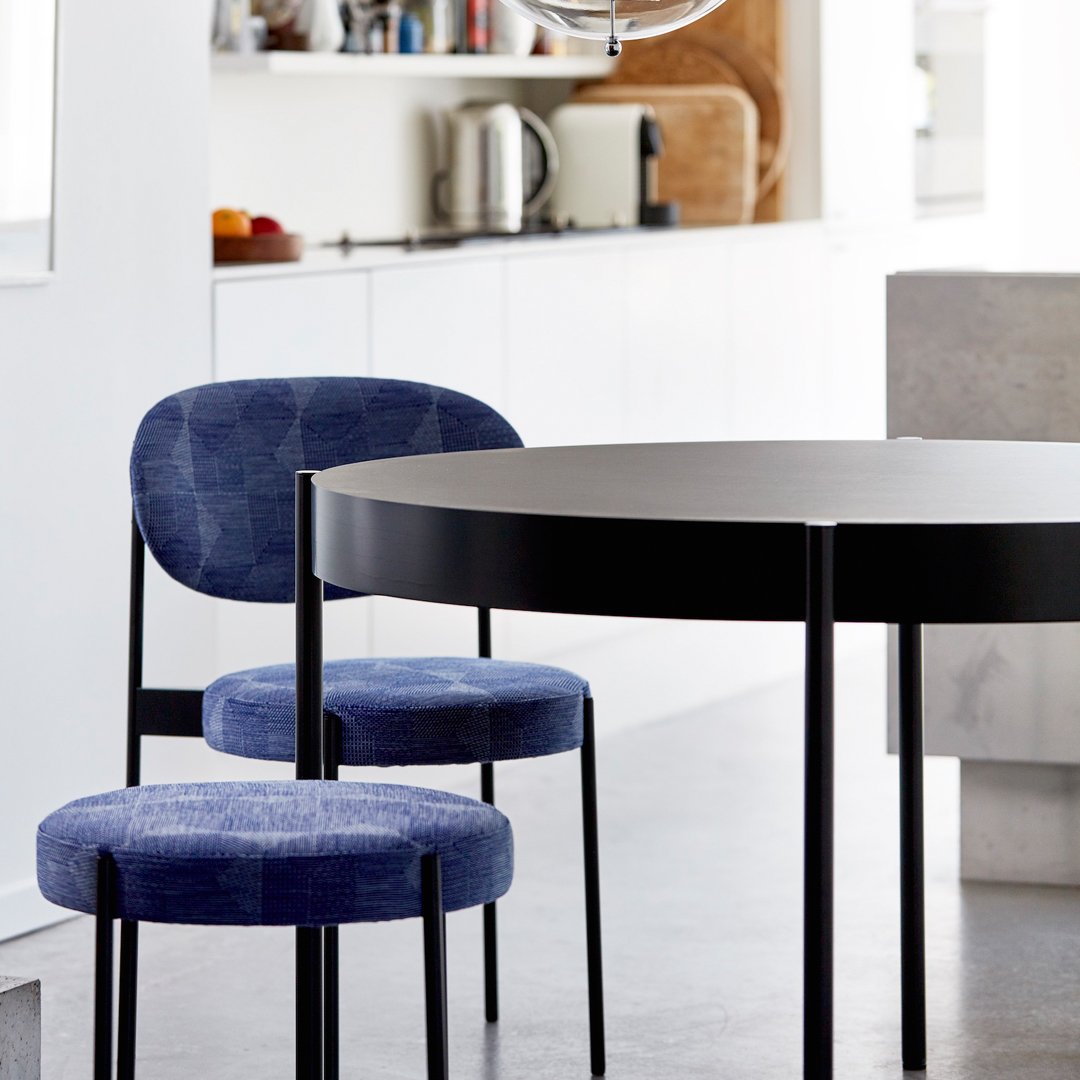 Modern black round table with two blue patterned chairs in a stylish dining space.