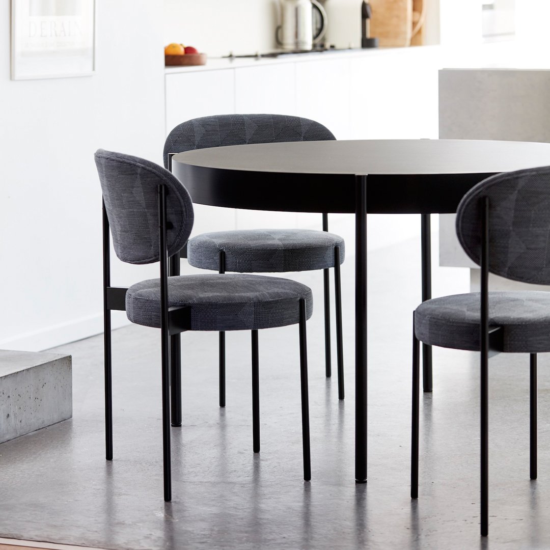 Modern black round dining table with four stylish gray upholstered chairs in a minimalist setting.