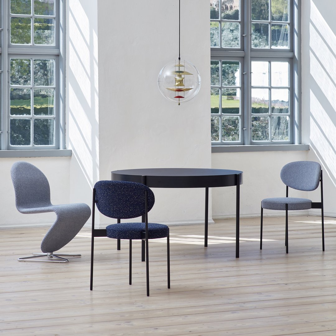 Modern dining room featuring a sleek black table, gray and navy patterned chairs, with large windows and natural light.