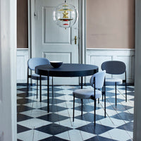 Round black dining table with gray patterned chairs on a black and white checkered floor. Elegant modern interior design.