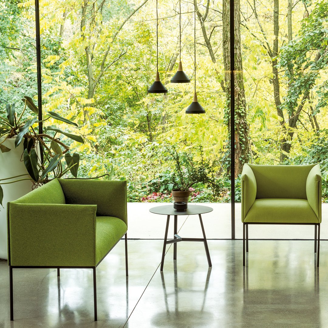 Modern green chairs with sleek black legs, complemented by a glass table in a bright, nature-inspired setting.
