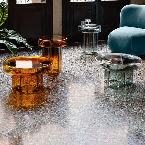 Colorful glass side tables in amber, clear, and blue hues create a vibrant and modern decor accent.