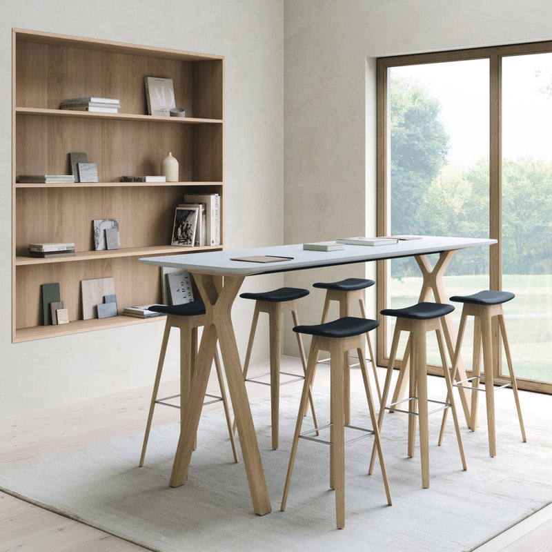 Modern white tabletop with natural wood legs and black cushioned stools, set in a light, airy room with minimal decor.