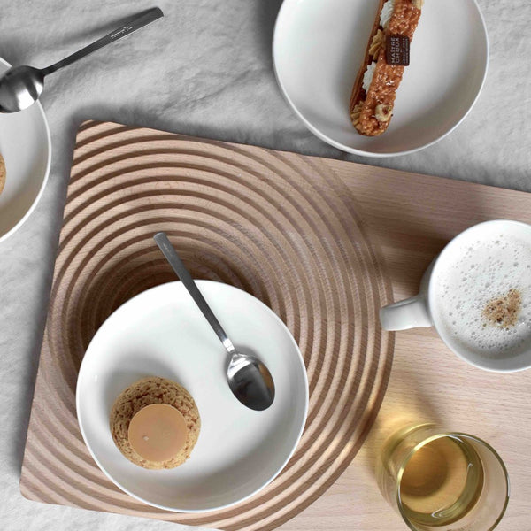Minimalist wood serving board with concentric circles, accompanied by white dishes and a warm neutral color palette.