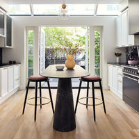 Sleek black marble table with pink stools, set in a bright, modern kitchen with white cabinetry and natural wood flooring.