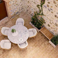 Round marble dining table with beige upholstered chairs, set against a rustic stone wall and warm, terracotta floor tiles.
