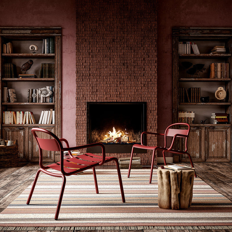 Red metal chairs on a striped rug, against a warm red wall and rustic wood shelves. Cozy, modern decor.