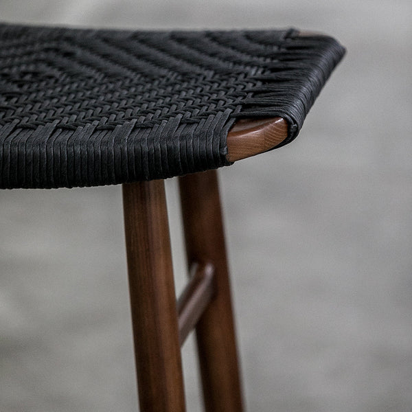 Black woven seat with intricate texture, paired with warm wooden legs, creating a stylish contrast.