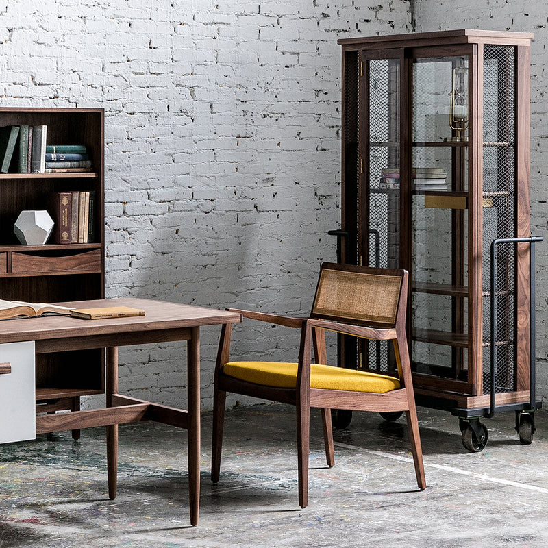 "Modern wooden desk with sleek lines, paired with a rattan chair featuring a pop of yellow, and a glass display cabinet."