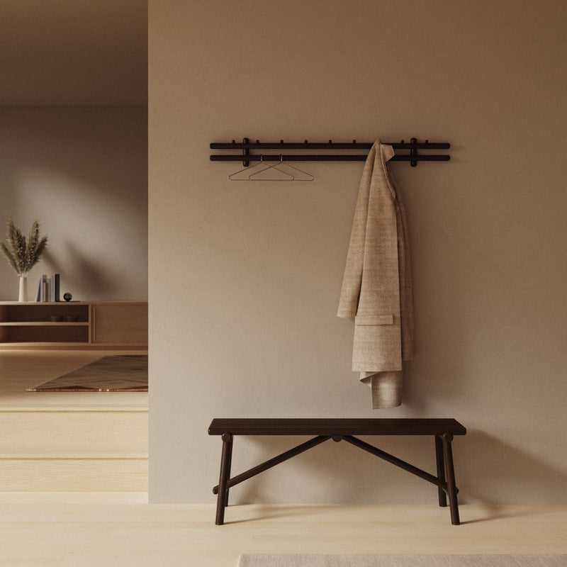 Neutral beige wall with a textured beige coat hanging on a black minimalist rack above a dark wooden bench.