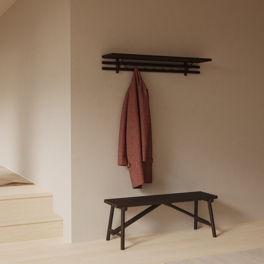 "Black wooden bench and rack with a rust-colored coat against a neutral beige wall, enhancing minimalist decor."