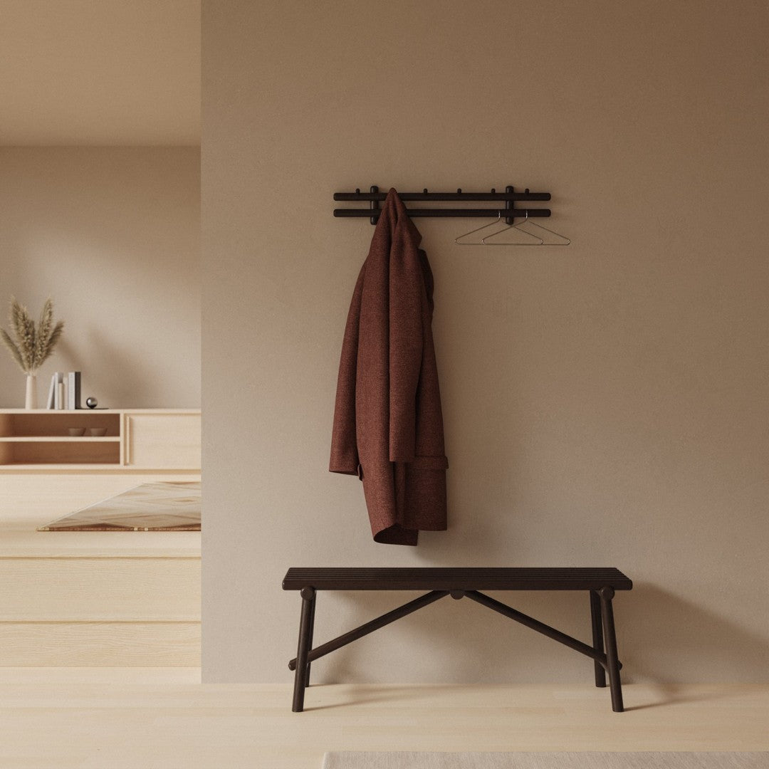 Dark brown bench with a textured finish, against a warm beige wall, featuring a deep burgundy coat hanging above.