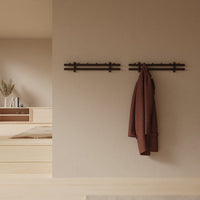 Brown coat hanging on dark wood hooks against a warm beige wall, featuring minimalist design and earthy tones.