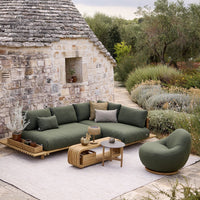 "Green upholstered sectional sofa with neutral cushions, set against a natural stone backdrop and lush greenery."