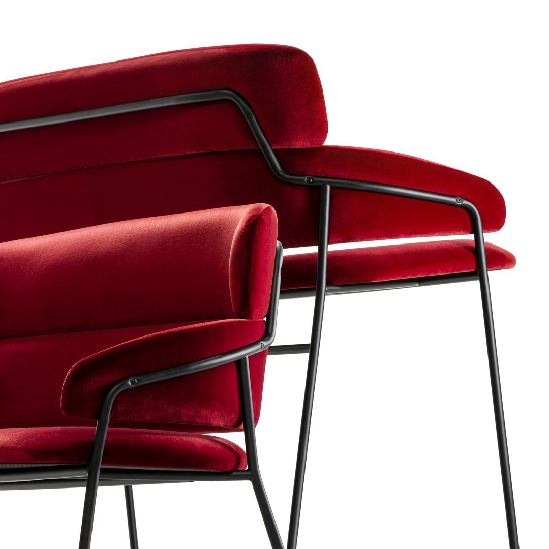 Red velvet armchairs with sleek black metal frames, featuring a smooth, modern design.