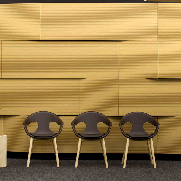 Three modern chairs in rich brown with curved backs, set against a warm, textured yellow wall.