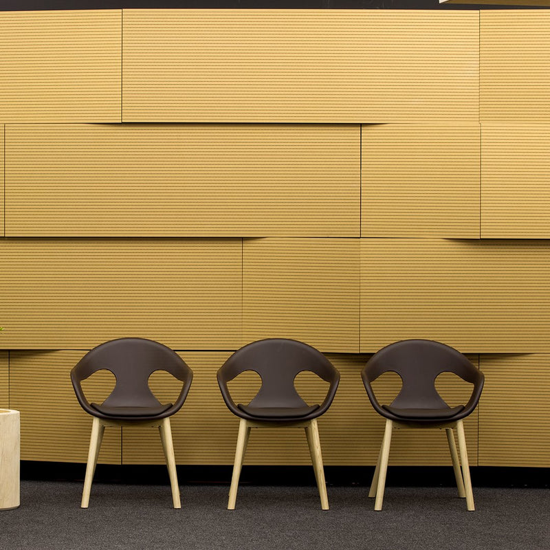 Three modern chairs in rich brown with curved backs, set against a warm, textured yellow wall.