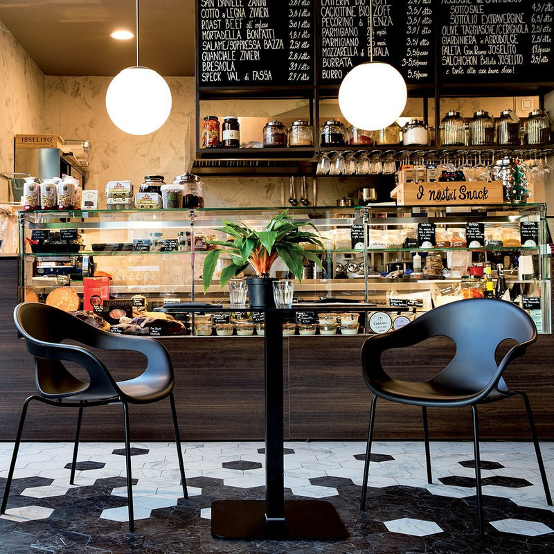 Black modern chairs with curved design on a hexagonal patterned floor, surrounded by a warm coffee shop ambiance.
