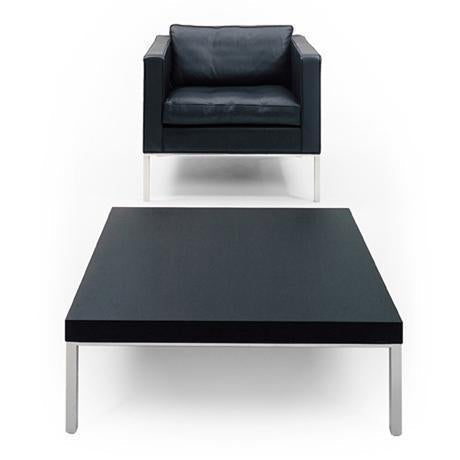Modern black armchair with plush cushions and sleek flat black coffee table, both featuring minimalistic silver legs.