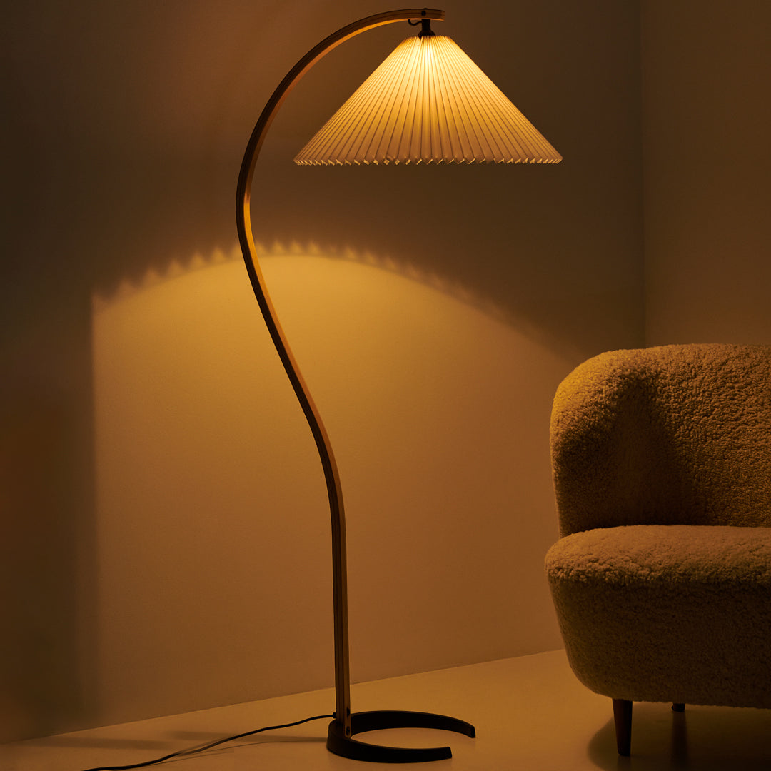 Elegant floor lamp with a creamy pleated shade and a sleek curved wooden base, casting a warm golden glow.