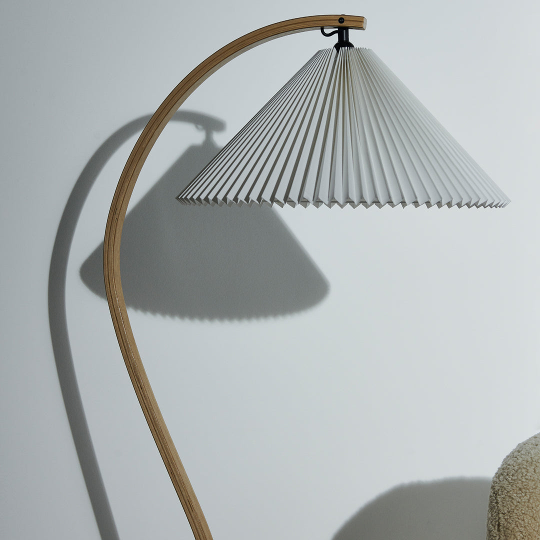 White pleated lamp shade with a natural wood arch stand, creating a modern and minimalist aesthetic.