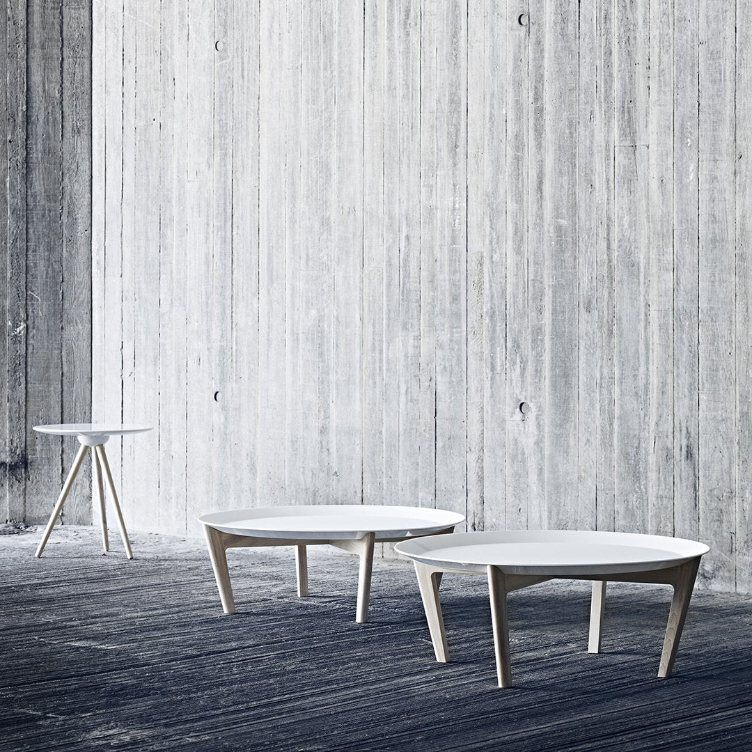 Modern white coffee tables with minimalist design set against a textured gray wall and dark wood flooring.