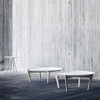 Modern white coffee tables with minimalist design set against a textured gray wall and dark wood flooring.