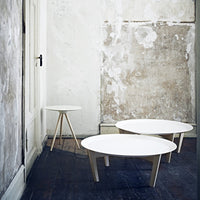 Three minimalist round coffee tables with white tops and natural wood legs, set against a textured wall.