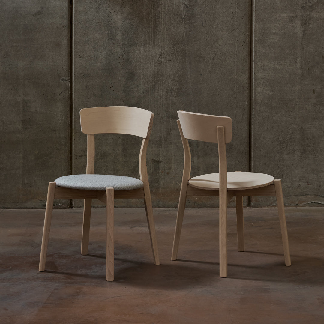 Pair of minimalist wooden chairs in natural wood finish with soft gray upholstery and simple, clean lines.