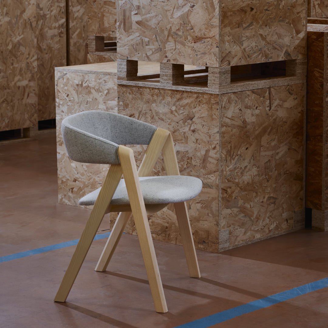 Light gray upholstered chair with minimalist design and natural wood legs, set against an industrial backdrop.