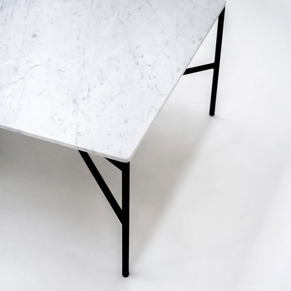 White marble tabletop with subtle gray veining, paired with sleek black metal legs on a neutral background.