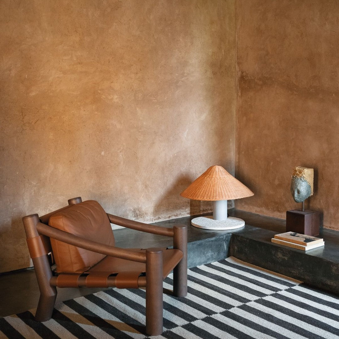 Brown leather chair with a striped black and white rug, complemented by a textured beige wall and earthy decor accents.