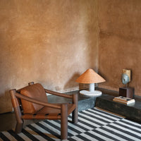 Brown leather chair with a striped black and white rug, complemented by a textured beige wall and earthy decor accents.