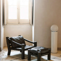 "Modern black leather armchair with a geometric design, paired with a matching ottoman in a bright, minimalistic setting."