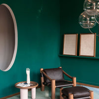 Teal walls with a circular cutout, brown wooden accents, and a sleek black chair create a modern, stylish space.