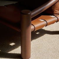 Brown leather lounge chair with a sleek, minimal design and contrasting light-colored fabric underneath.