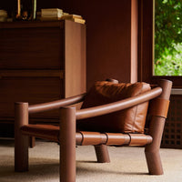Brown wooden lounge chair with a smooth leather cushion, featuring minimalist design and natural earthy tones.