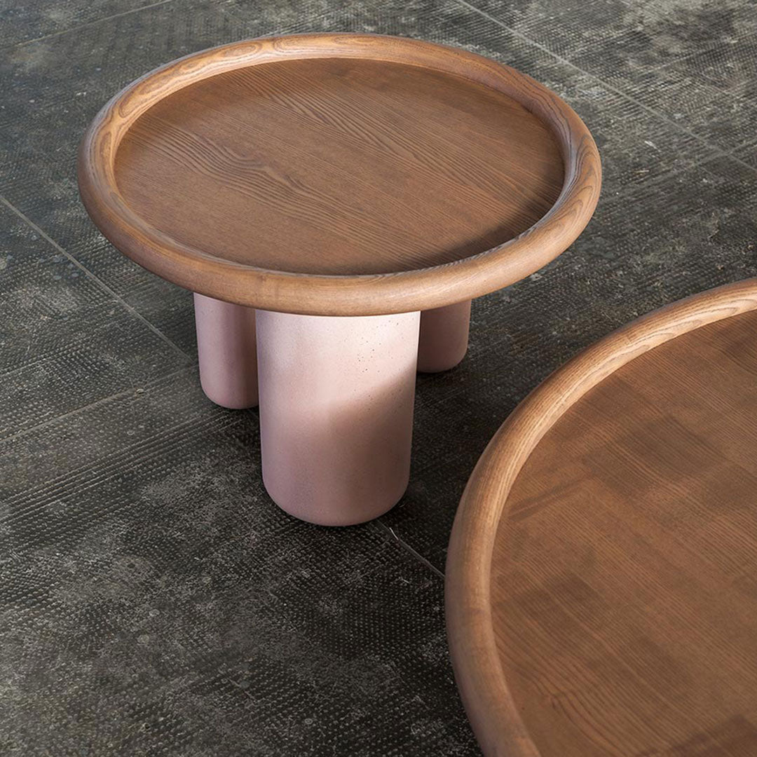 Round wooden coffee table with a light natural finish and soft pink cylindrical legs, showcasing a minimalist design.