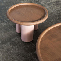 Round wooden coffee table with a light natural finish and soft pink cylindrical legs, showcasing a minimalist design.